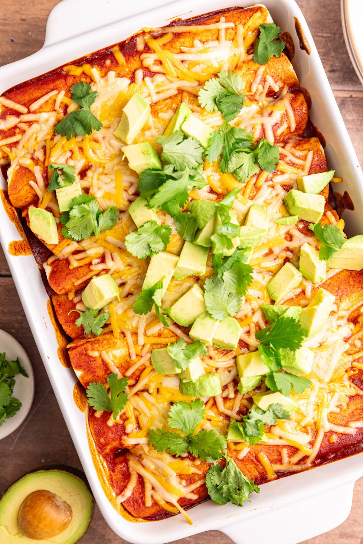 A dish of freshly cooked vegan rice and bean enchiladas, topped with diced avocado and cilantro leaves.