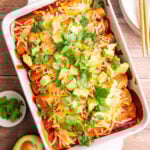 A dish of freshly cooked vegan rice and bean enchiladas, topped with diced avocado and cilantro leaves.