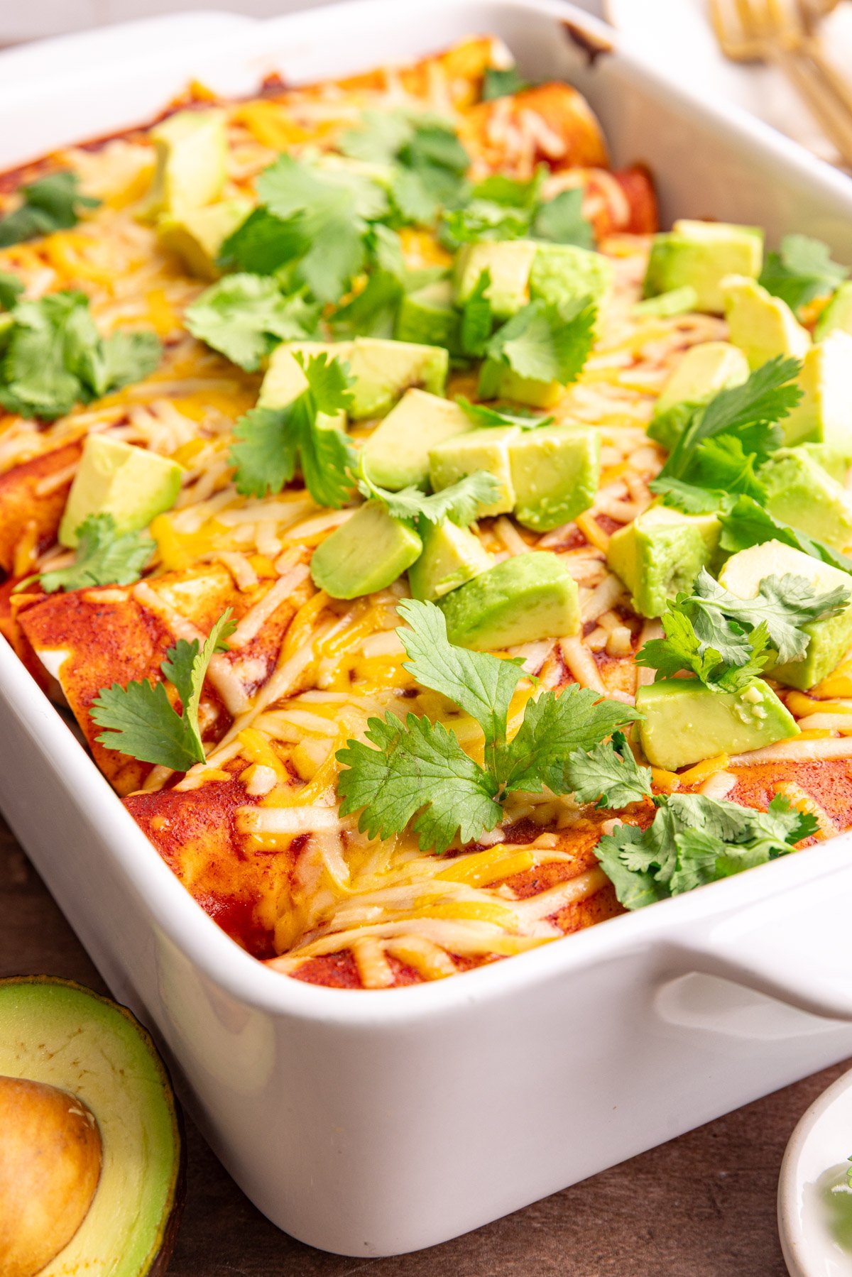 A dish of freshly cooked vegan rice and bean enchiladas, topped with diced avocado and cilantro leaves.
