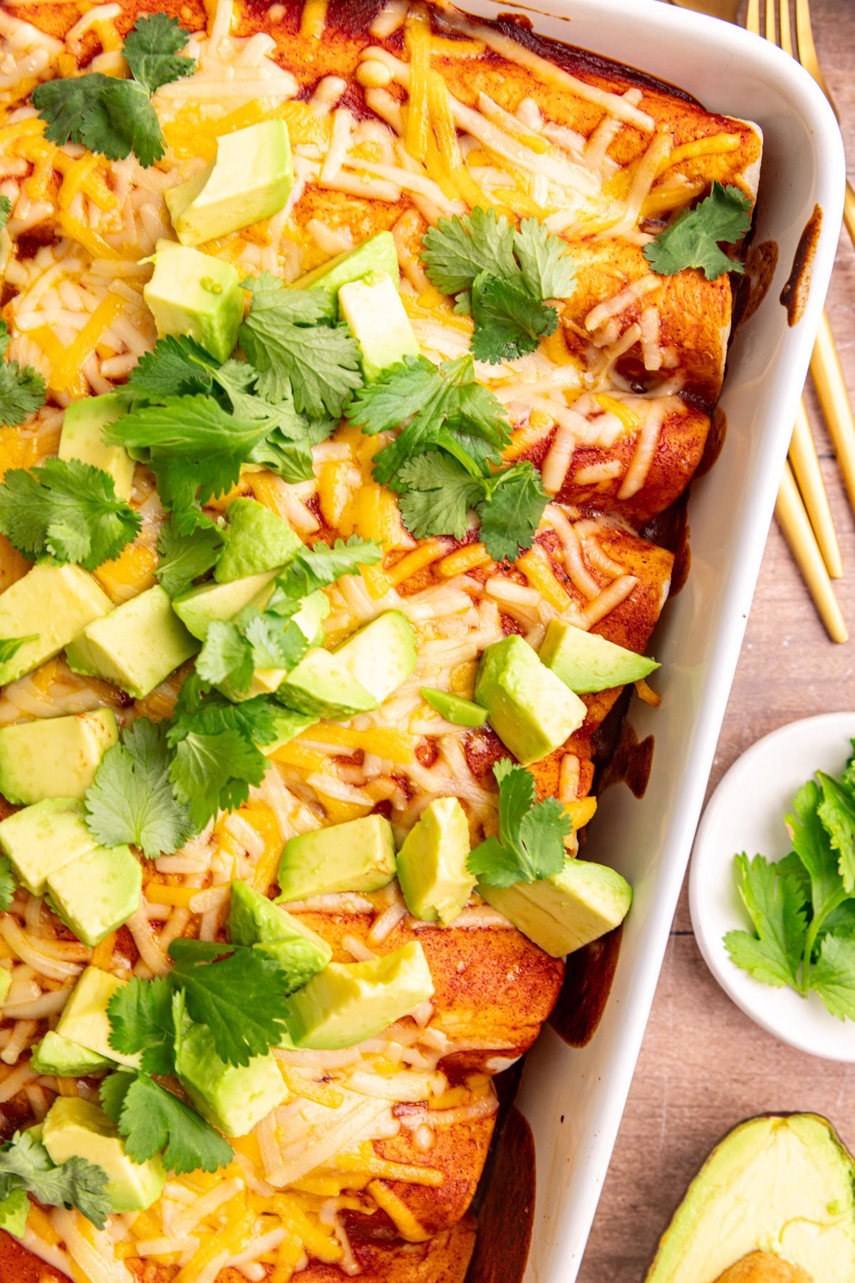 A dish of freshly cooked vegan rice and bean enchiladas, topped with diced avocado and cilantro leaves.