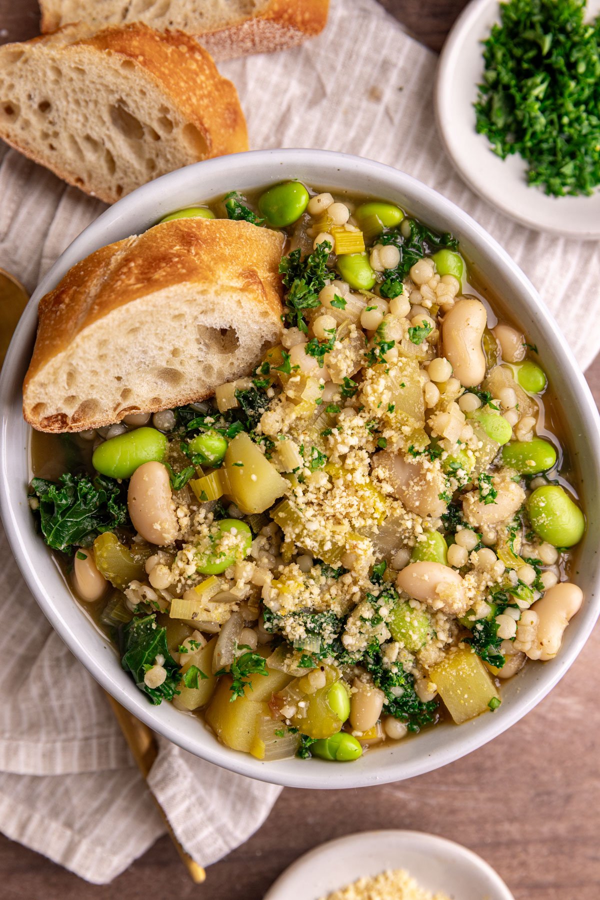 A bowl of white minestrone soup, with a piece of bread, garnished with vegan parmesan.