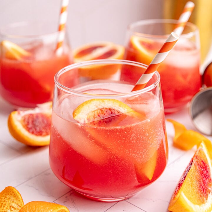 An aperol spritz mocktail garnished with a blood orange wedge and orang and white striped straw.