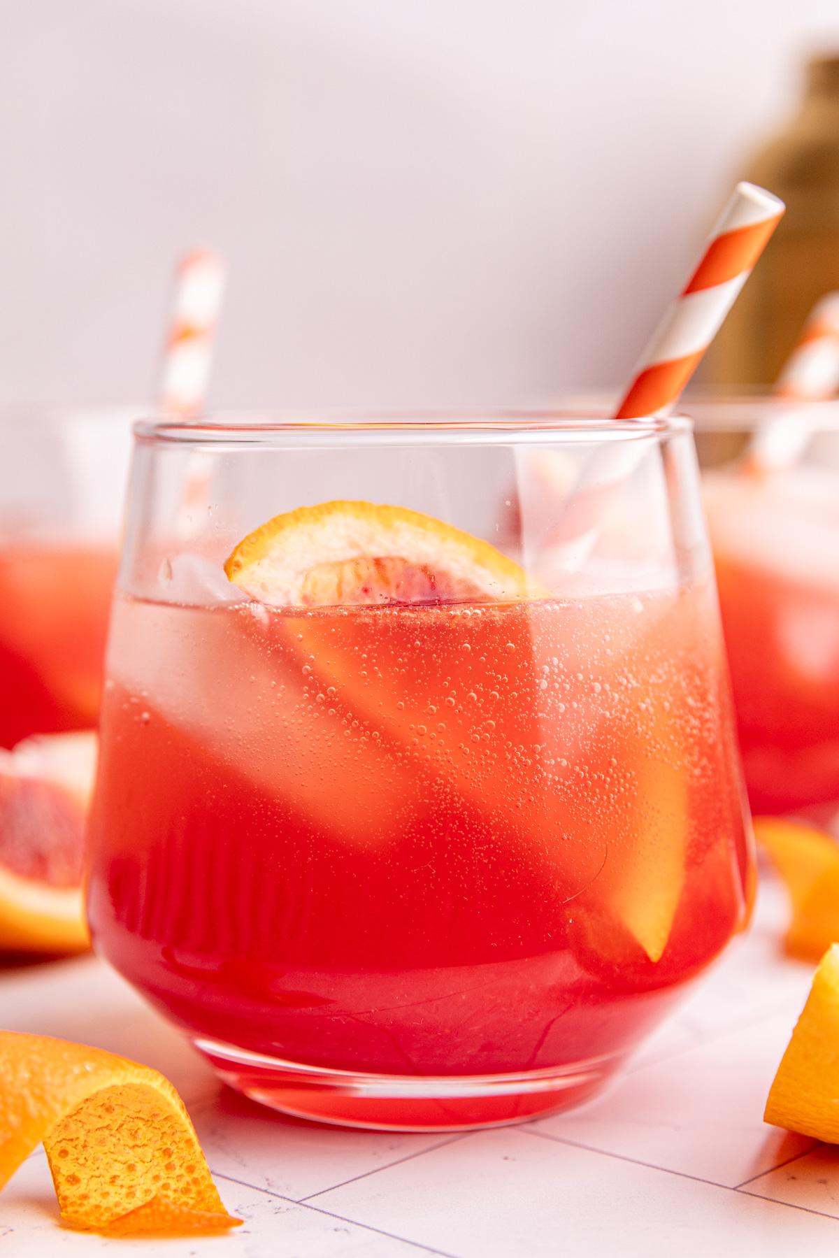 An aperol spritz mocktail garnished with a blood orange wedge and orang and white striped straw.