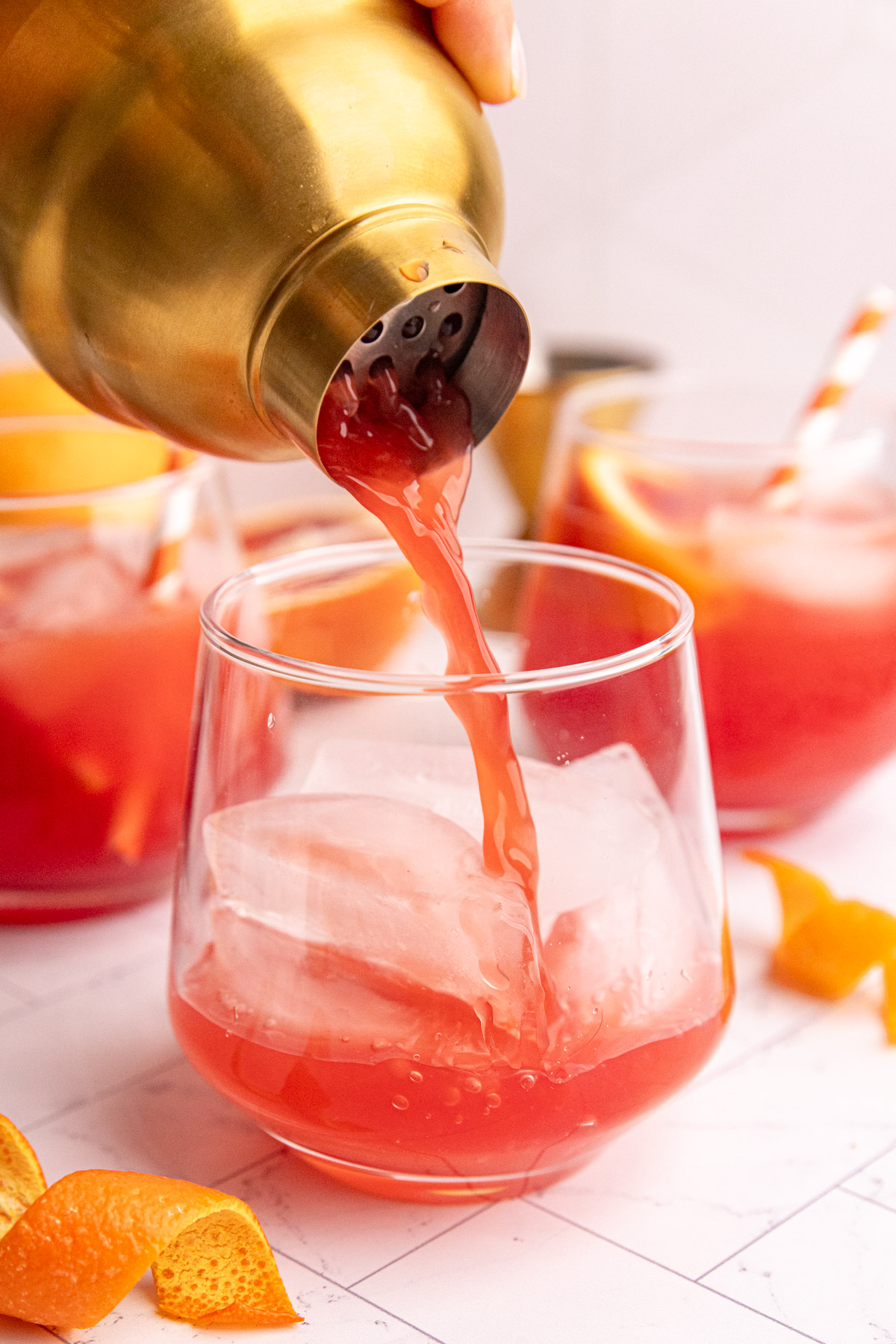 The orange and cranberry juice mixture being strained through a cocktail shaker into a glass.