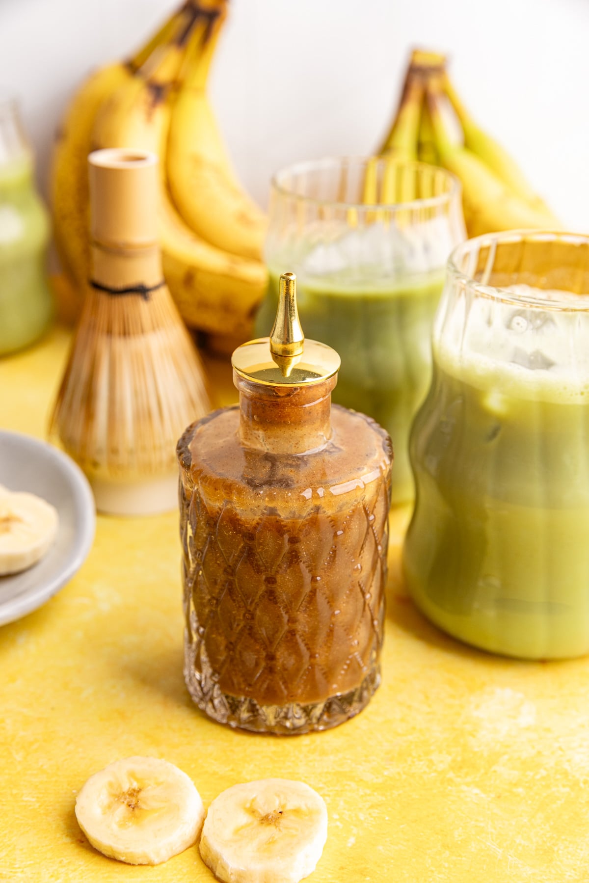A jar of banana simple syrup, next to a few glasses of banana matcha.