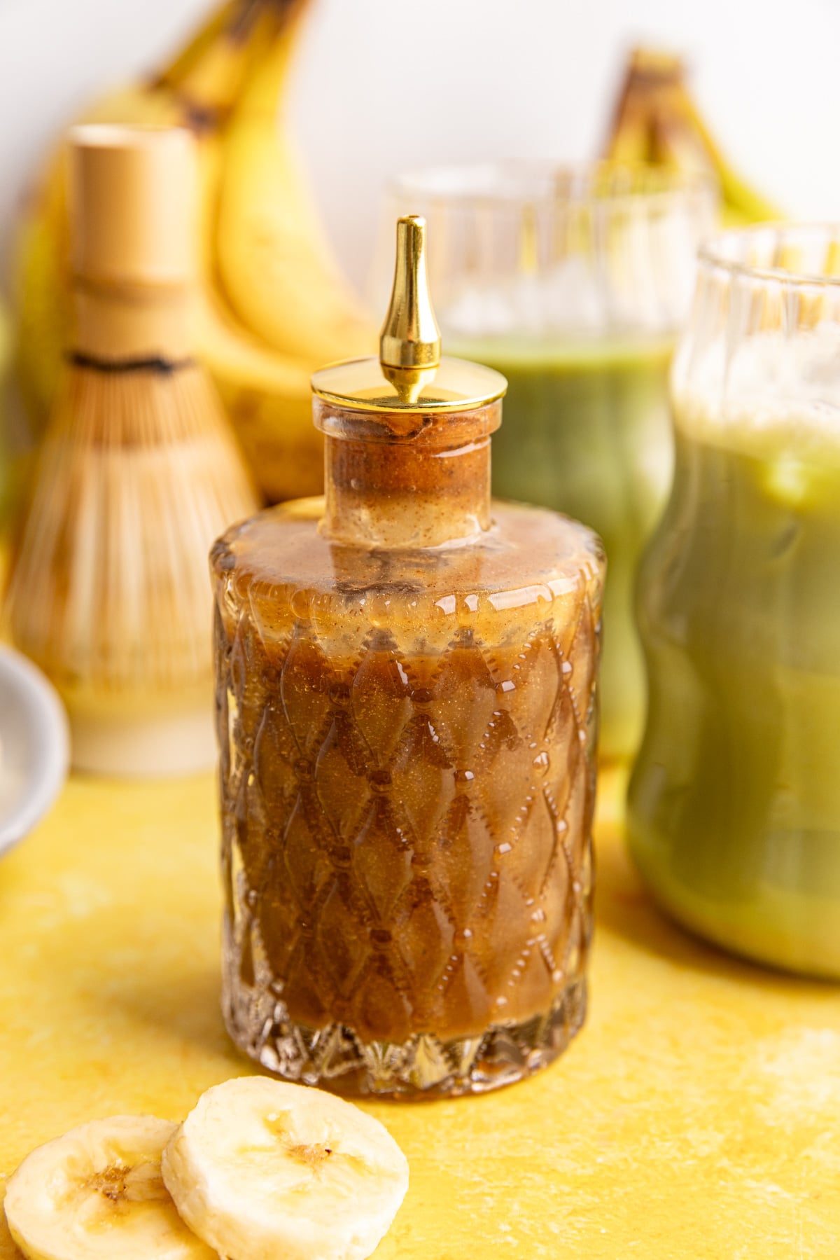 A jar of banana syrup, next to a few glasses of banana matcha.