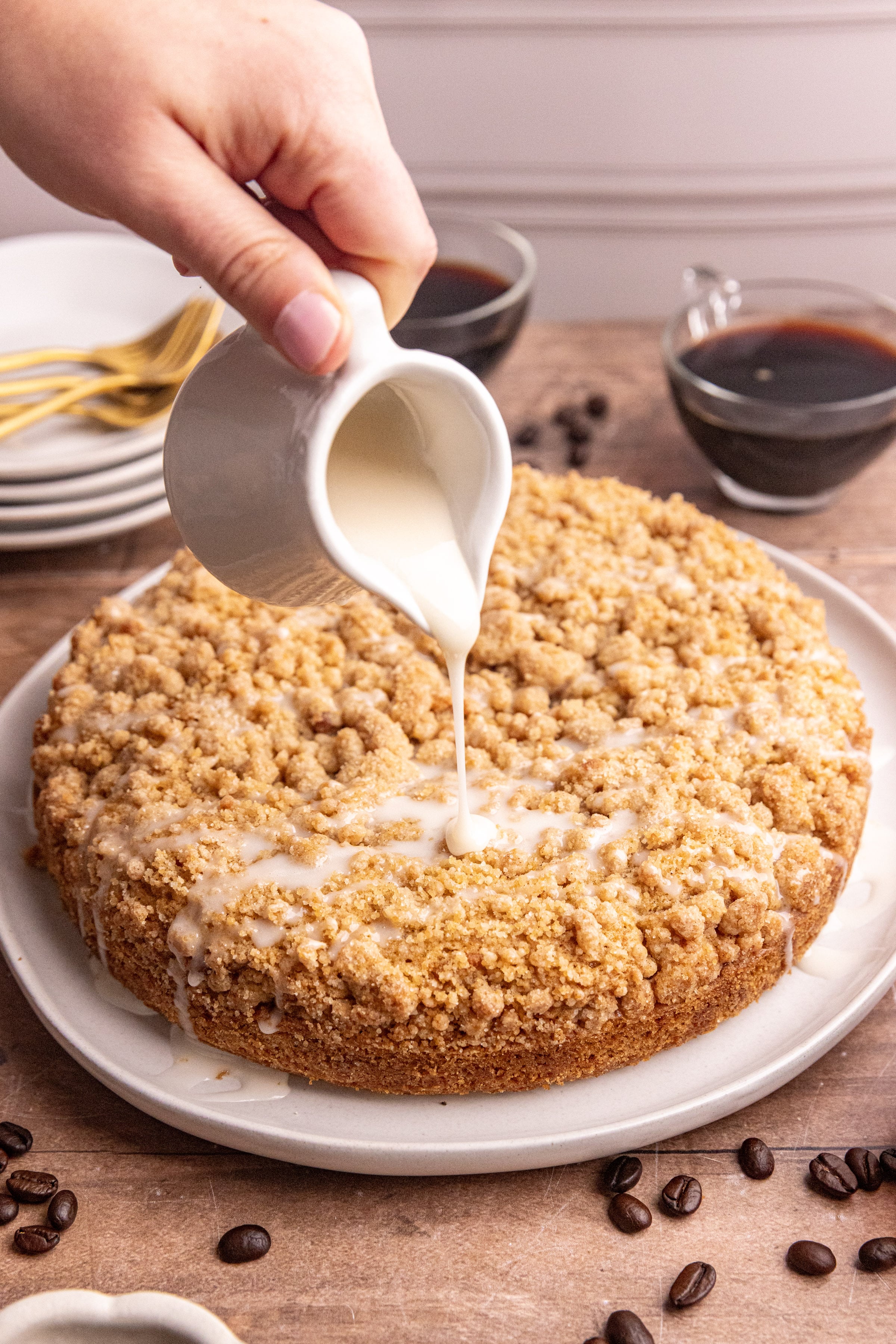 A platter of vegan cinnamon streusel coffee cake being drizzled with glaze.
