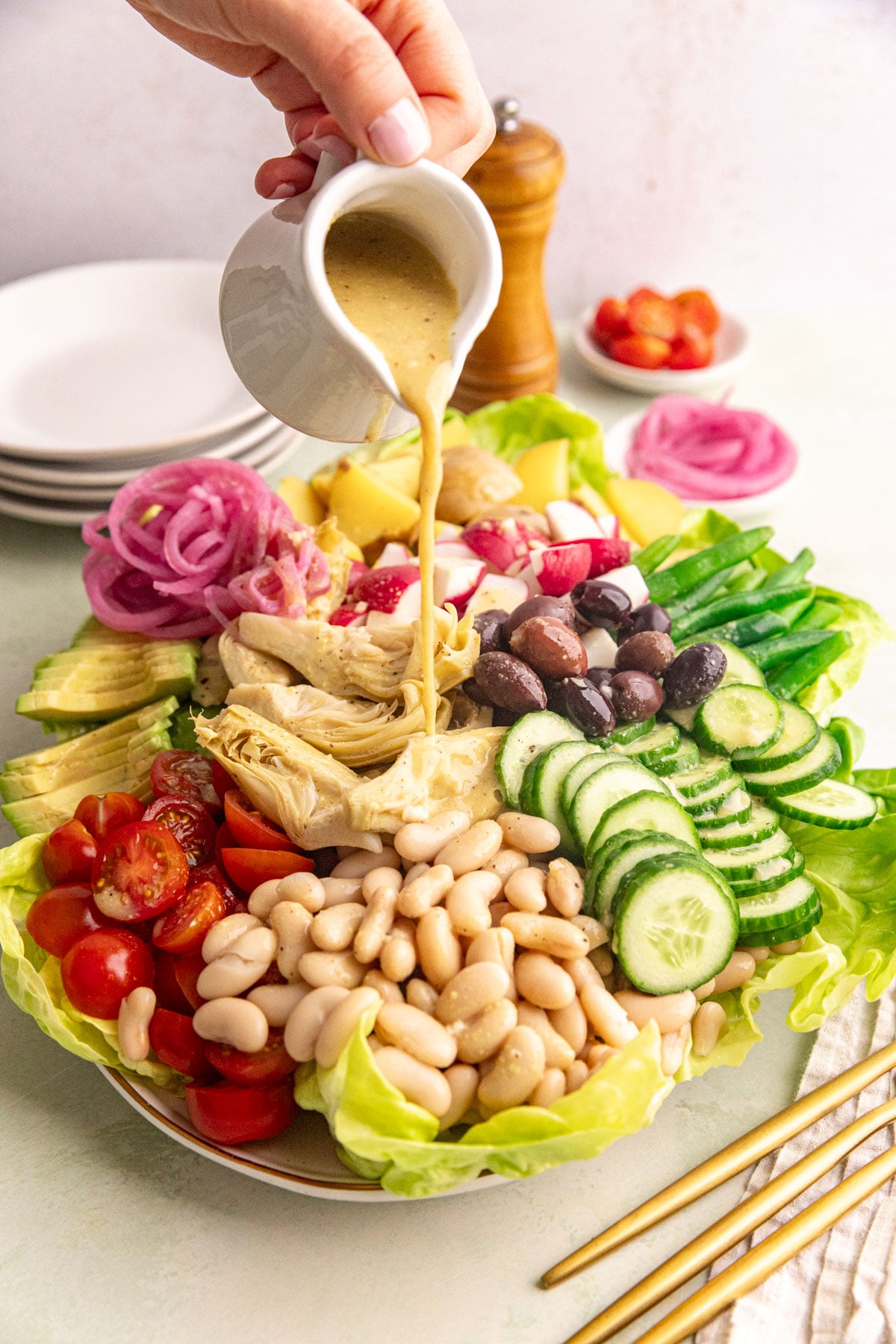 A platter of vegan Nicoise salad being drizzled with dressing.