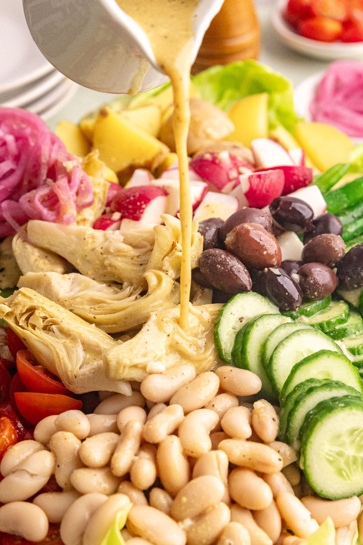 A platter of vegan Nicoise salad being drizzled with dressing.