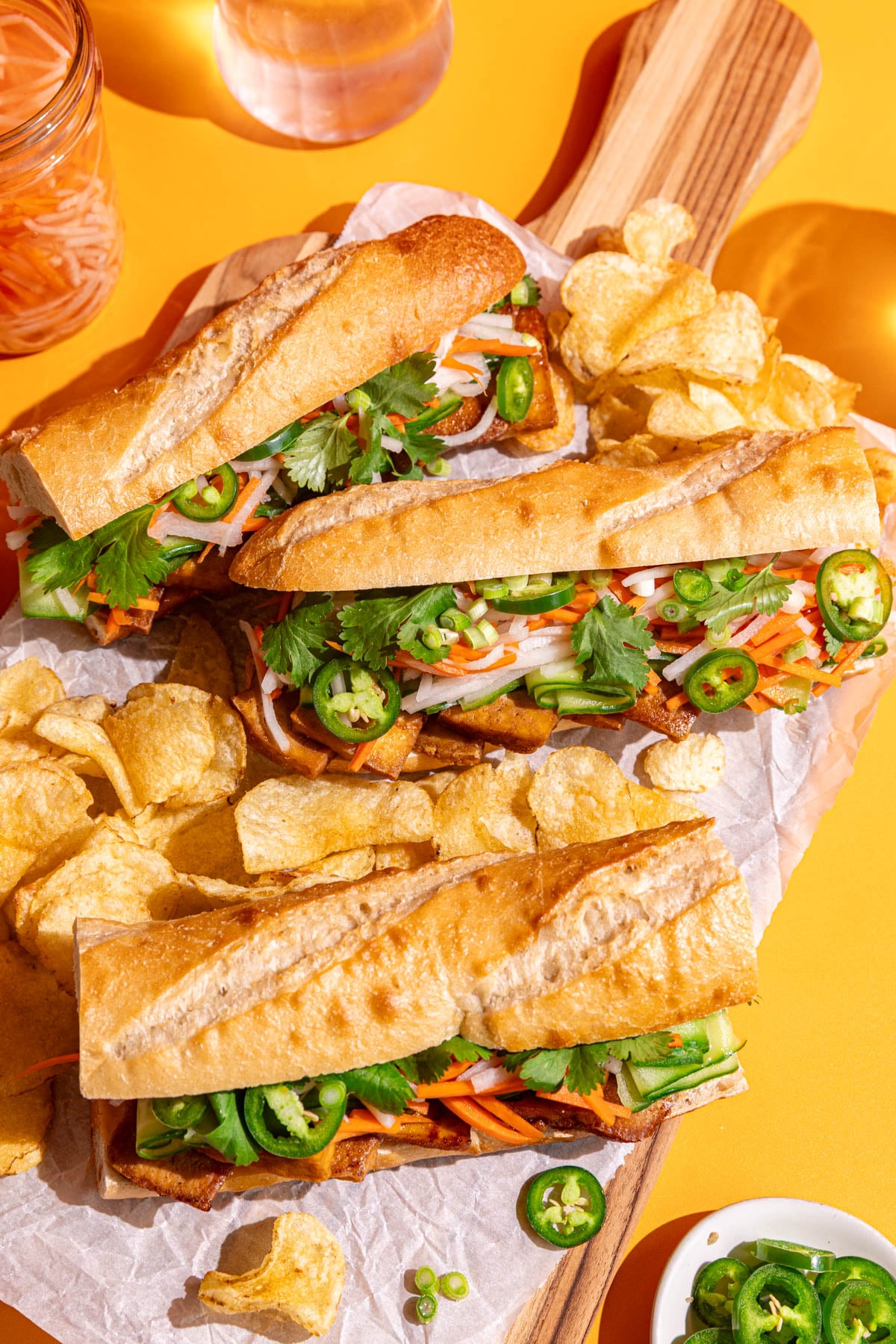 Three Banh Mi tofu sandwiches on a board with chips.