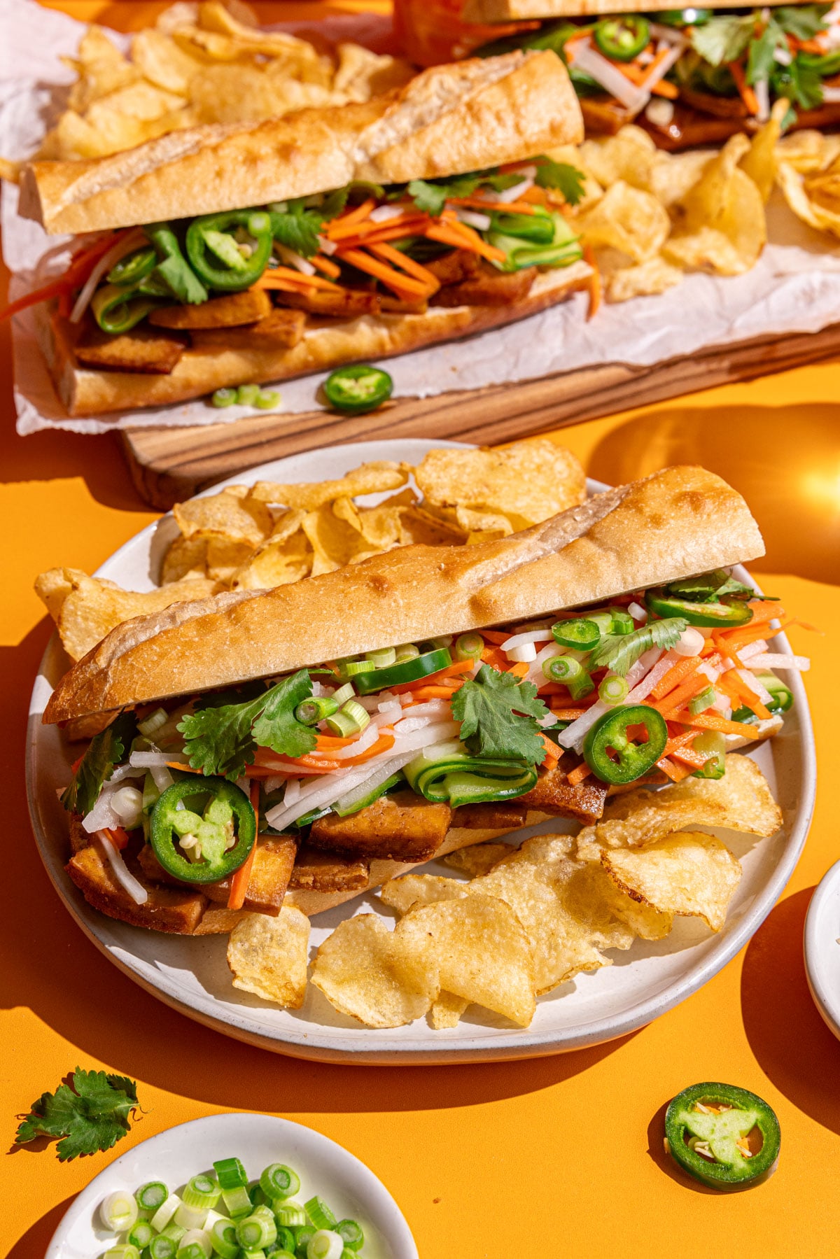 A Banh Mi tofu sandwich on a plate with potato chips.