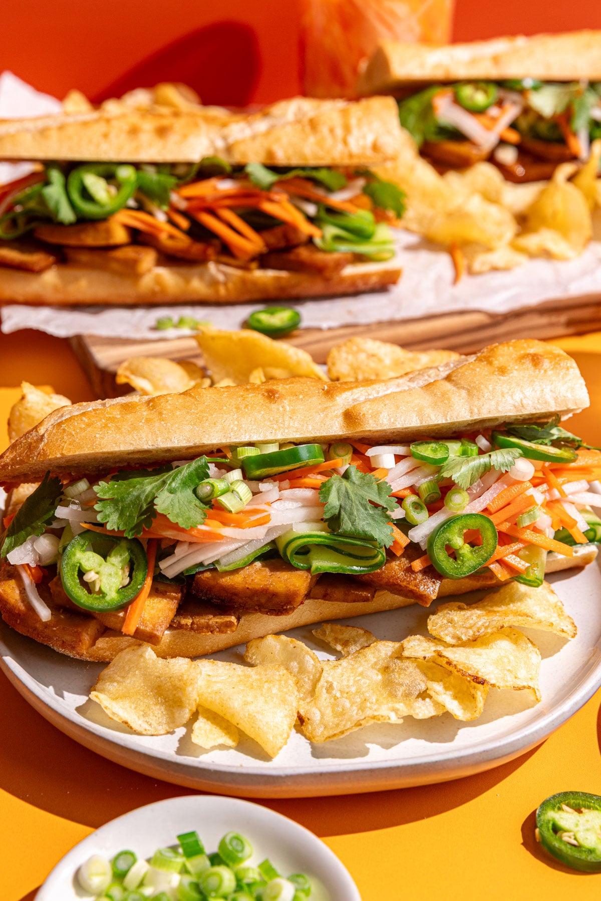 A Banh Mi tofu sandwich on a plate with potato chips.