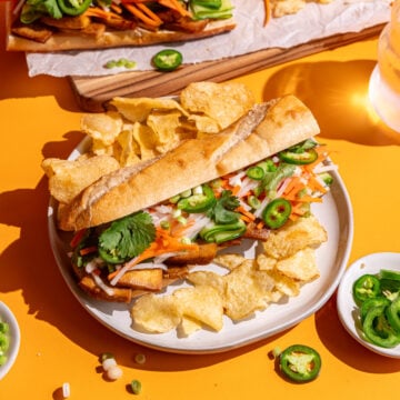 A Tofu Banh Mi sandwich on a plate with potato chips.
