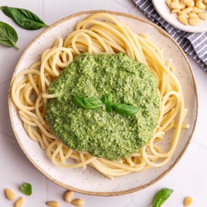 A bowl of spaghetti topped with Vegan oil free pesto, garnished with a basil leaf.