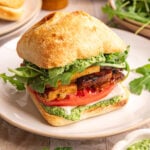 A plate with a vegan pesto sandwich, on a ciabatta roll, with pesto, tofu, and fresh veggies.