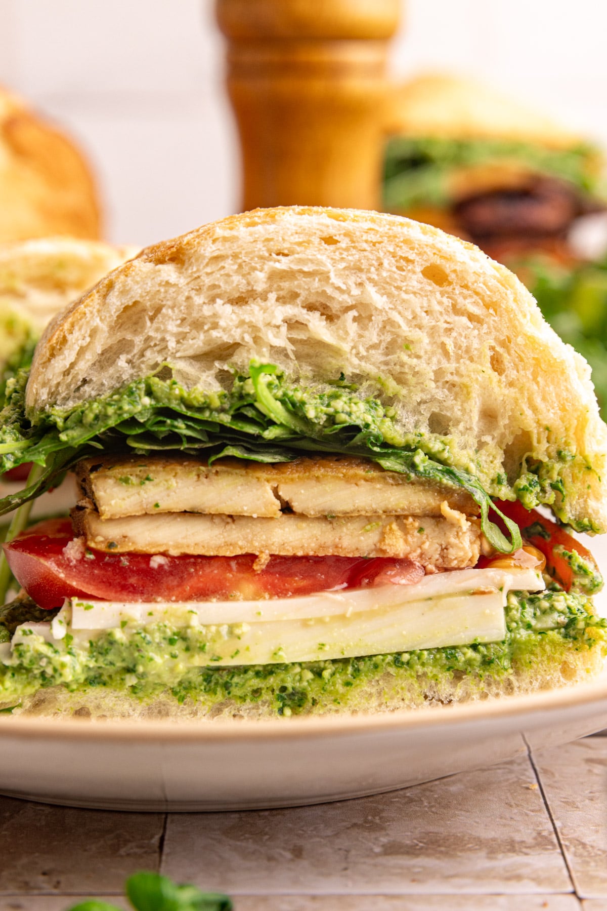 A vegan pesto sandwich, sliced in half to see the fluffy ciabatta, tofu, and pesto.