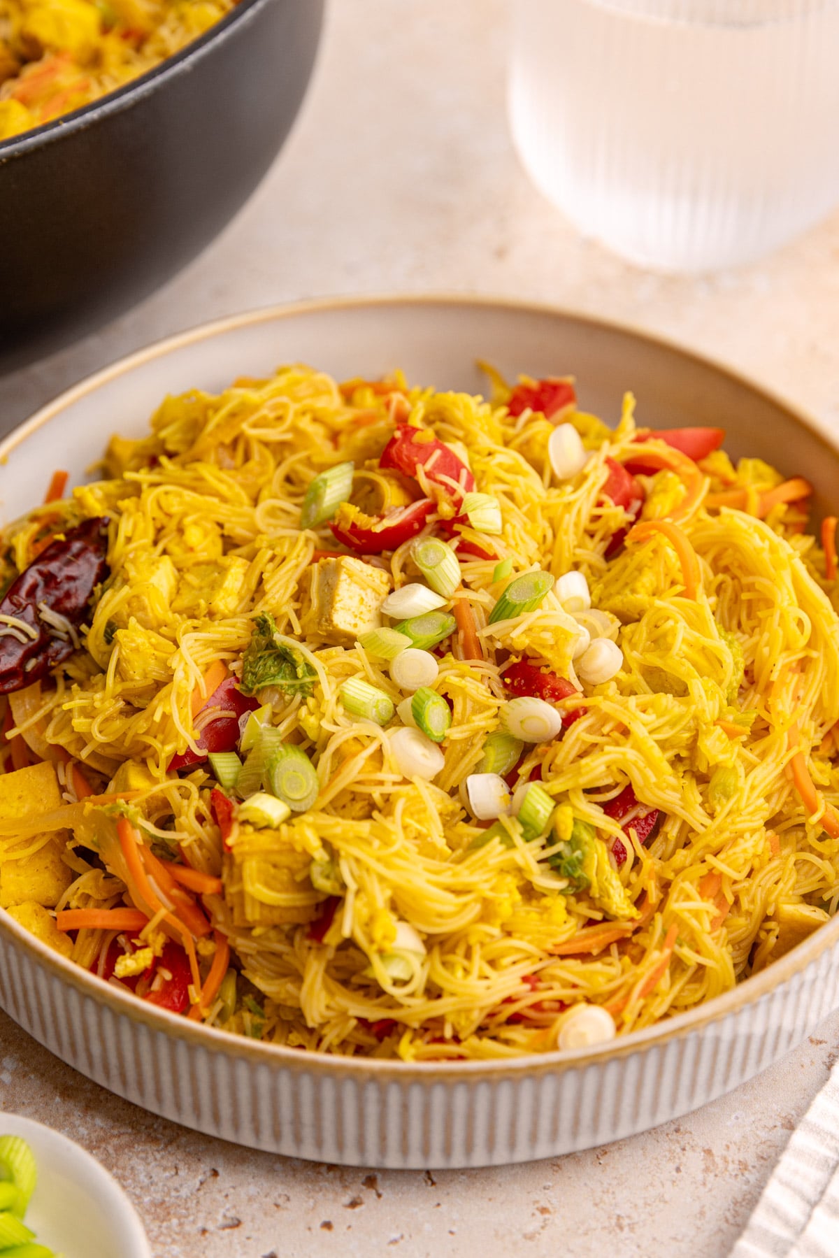 A bowl of vegan Singapore noodles with tofu, garnished with scallions.