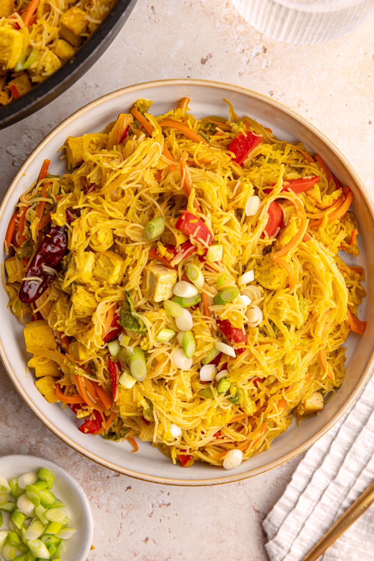 A bowl of vegan Singapore noodles with tofu, garnished with scallions.