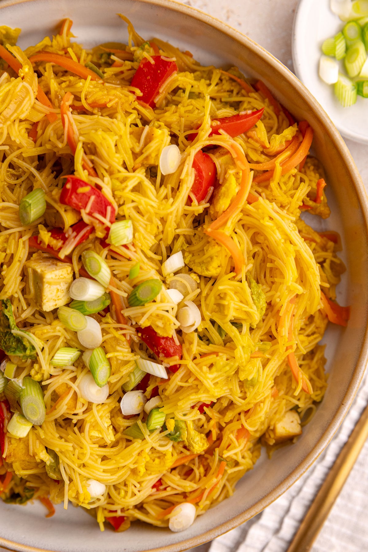 A bowl of vegan Singapore noodles with tofu, garnished with scallions.