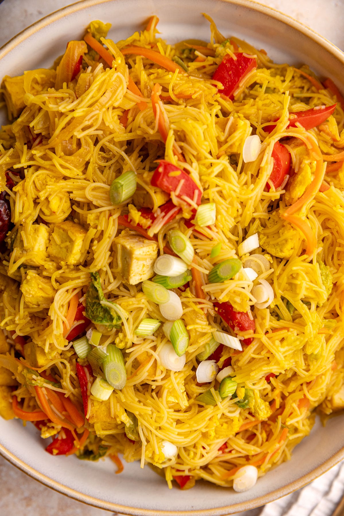 A bowl of vegan Singapore noodles with tofu, garnished with scallions.