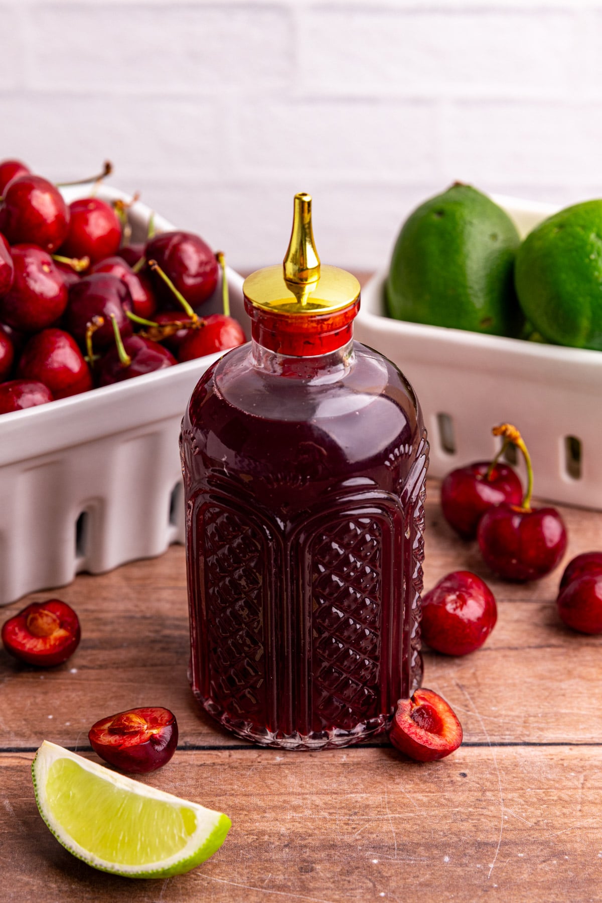 A bottle of cherry simple syrup, with fresh cherries and limes.