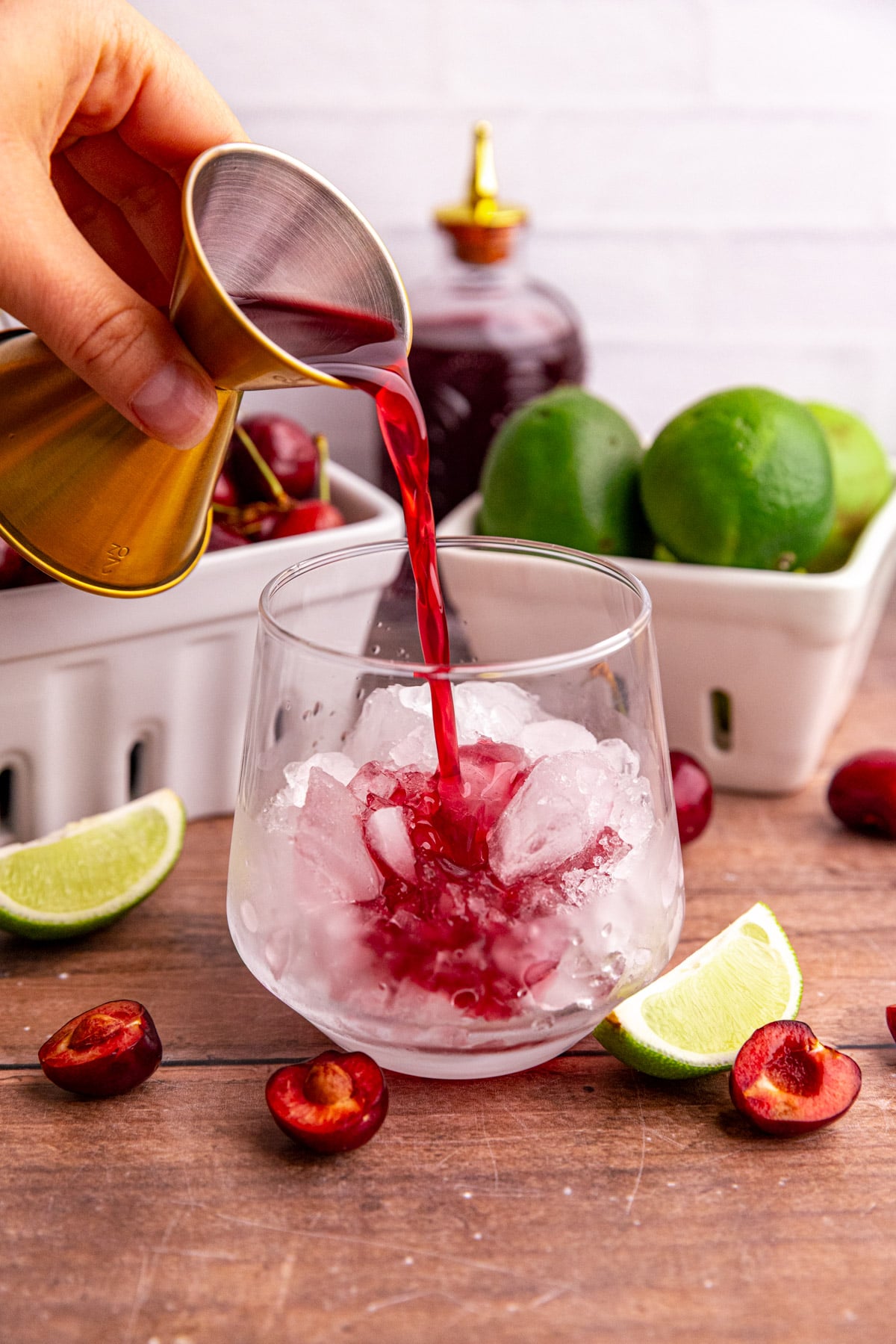 Cherry simple syrup being poured into a glass with ice to make a mocktail.