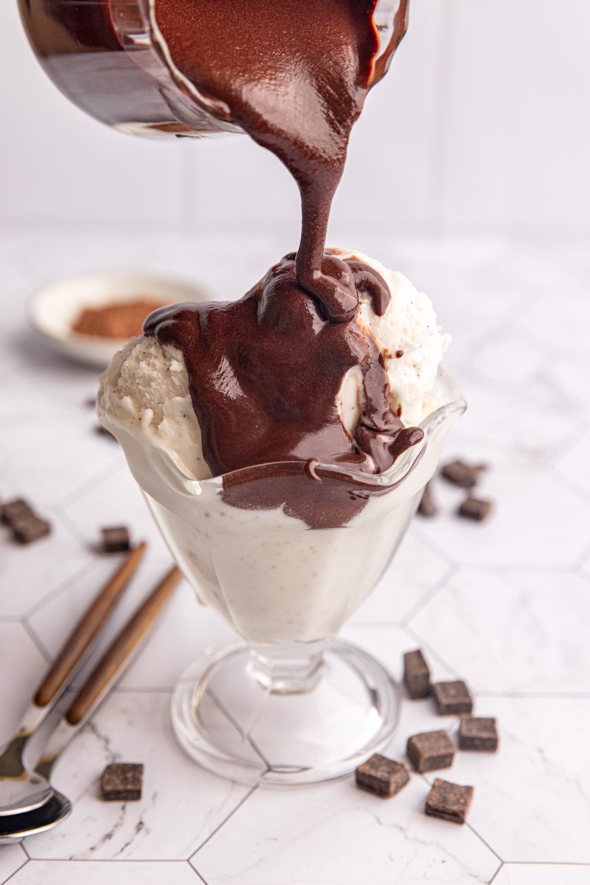 Chocolate simple syrup being poured onto a bowl of ice cream.