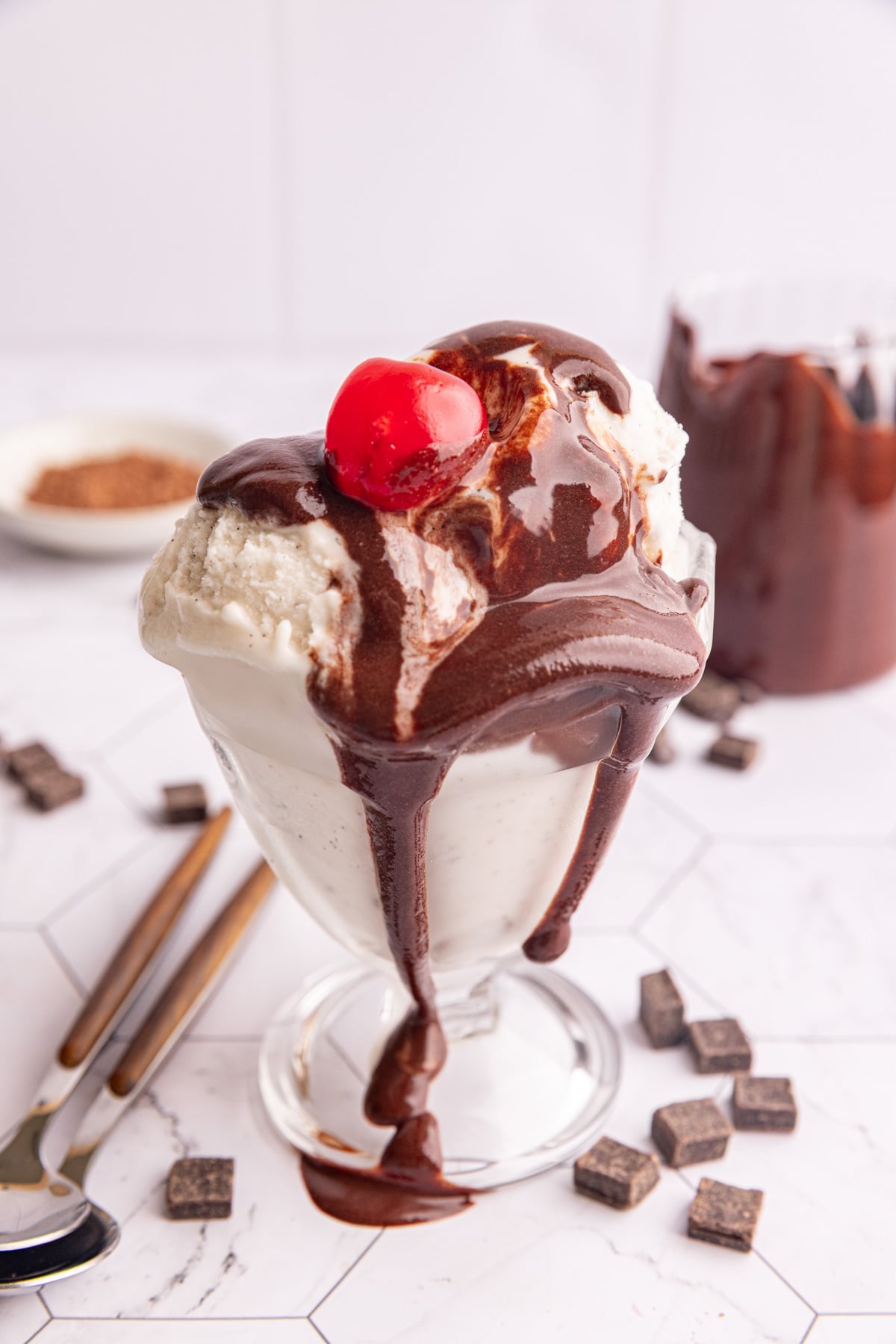 Chocolate simple syrup dripping off of a bowl of ice cream, with a cherry on top.