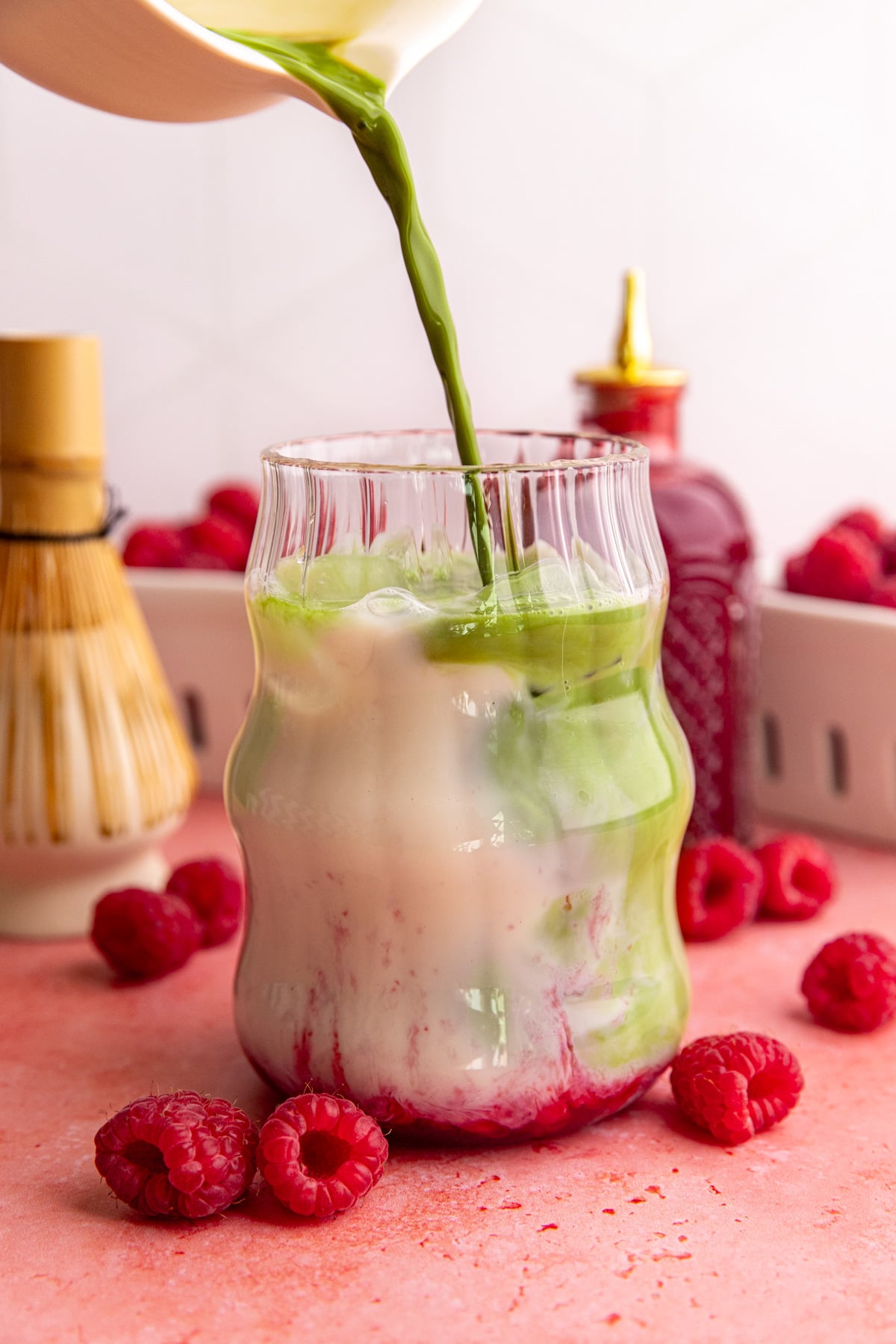 Matcha being poured into a glass with milk and raspberry syrup.