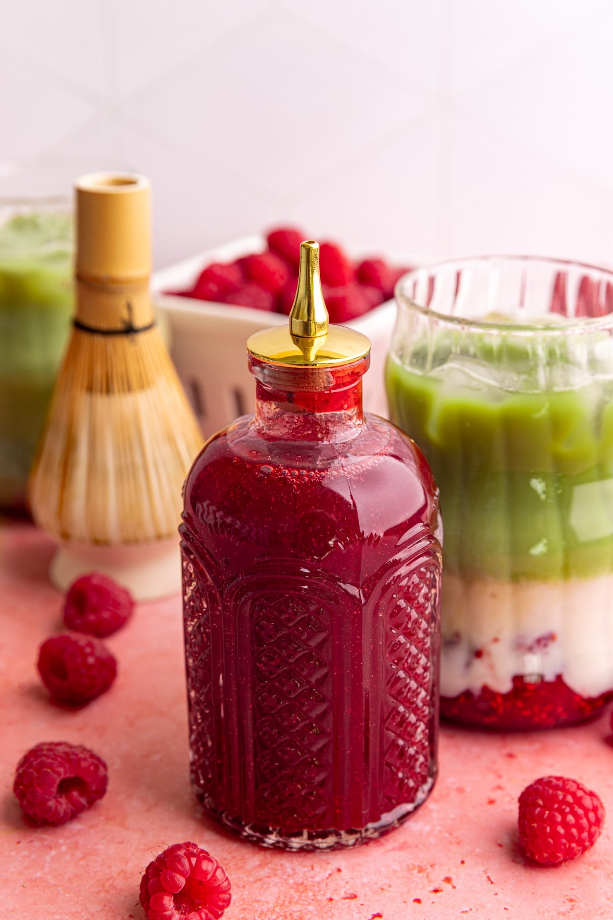 A bottle of raspberry simple syrup with a raspberry matcha latte.