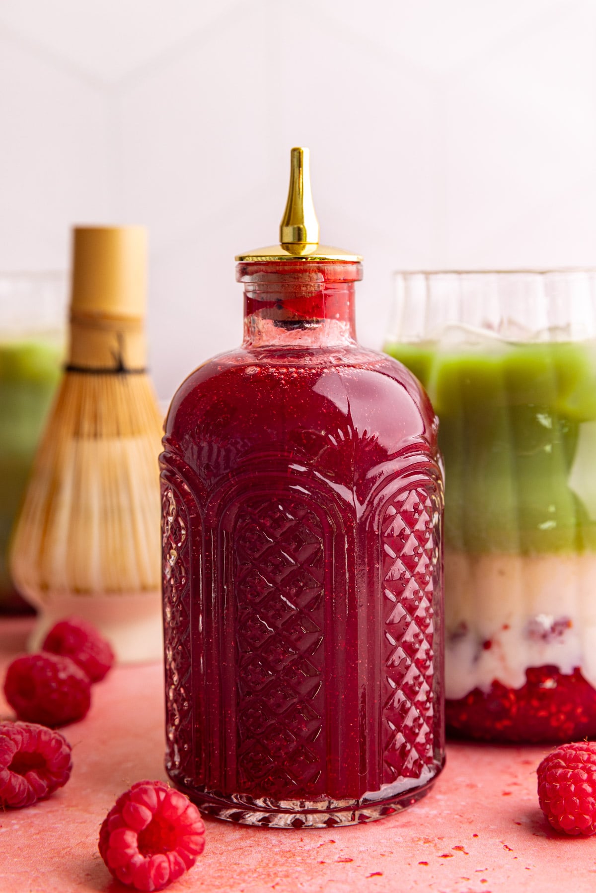 A bottle of raspberry simple syrup with a raspberry matcha latte.