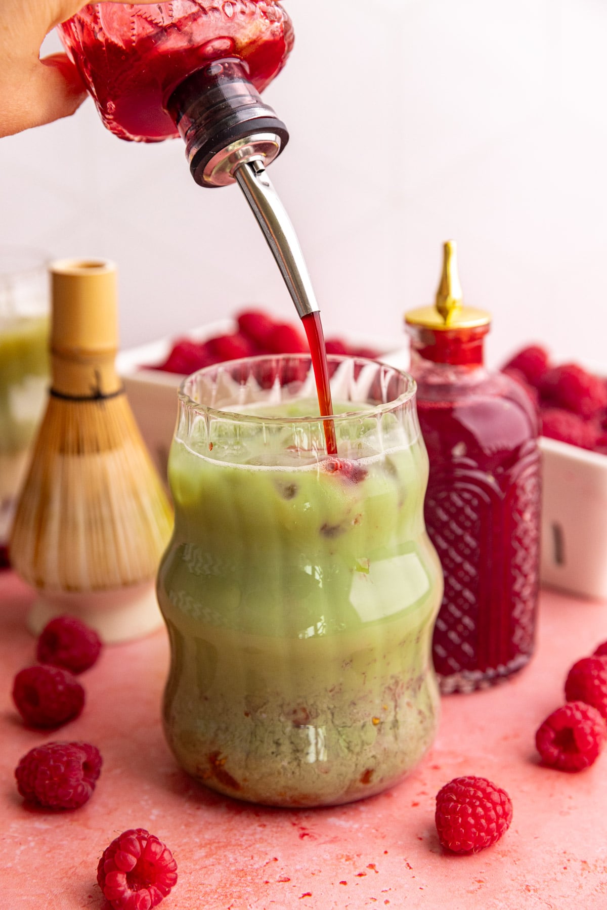 Raspberry simple syrup being poured into a raspberry matcha latte.