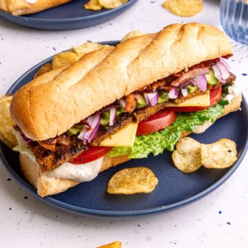A vegan chicken bacon ranch sandwich, on a plate with a few potato chips.