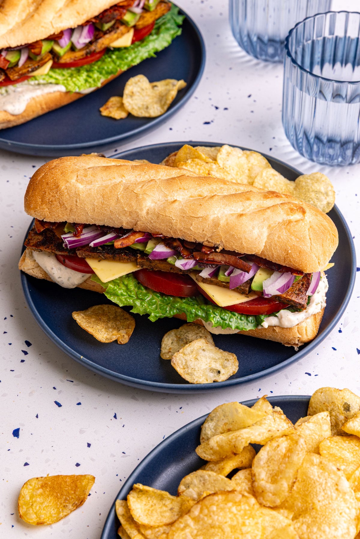 A vegan chicken bacon ranch sandwich, on a plate with a few potato chips.