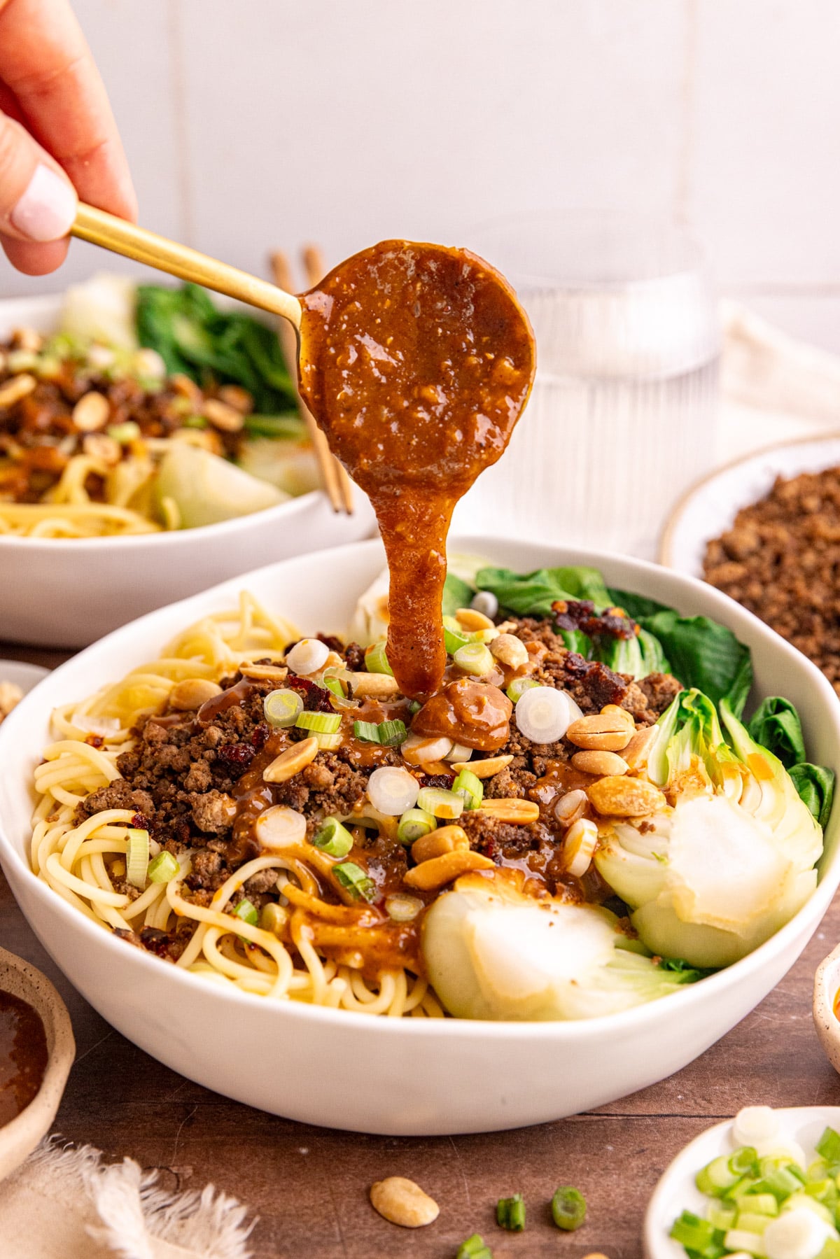 A spoon pouring sauce onto a bowl of dan dan noodles.