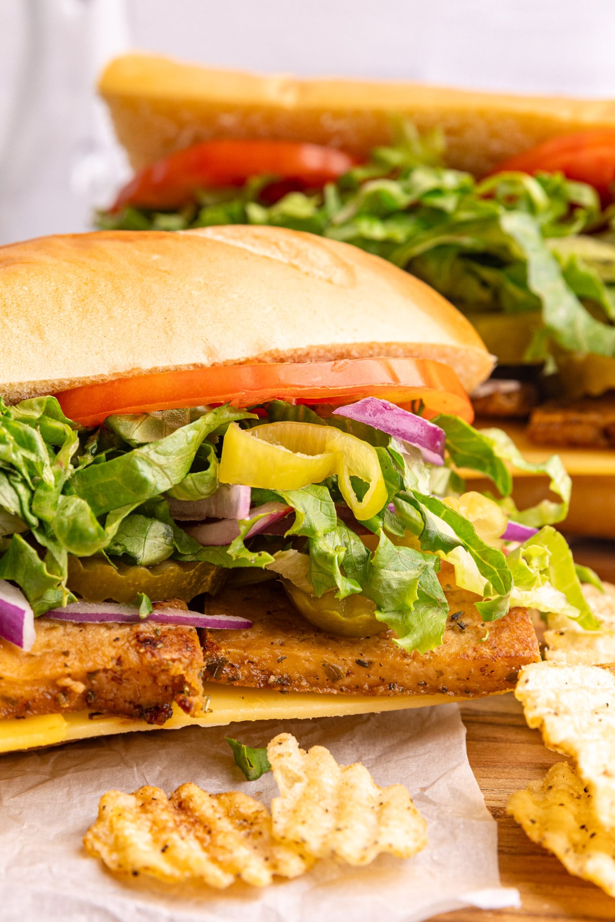 A vegan deli turkey sandwich on a baguette, with potato chips.