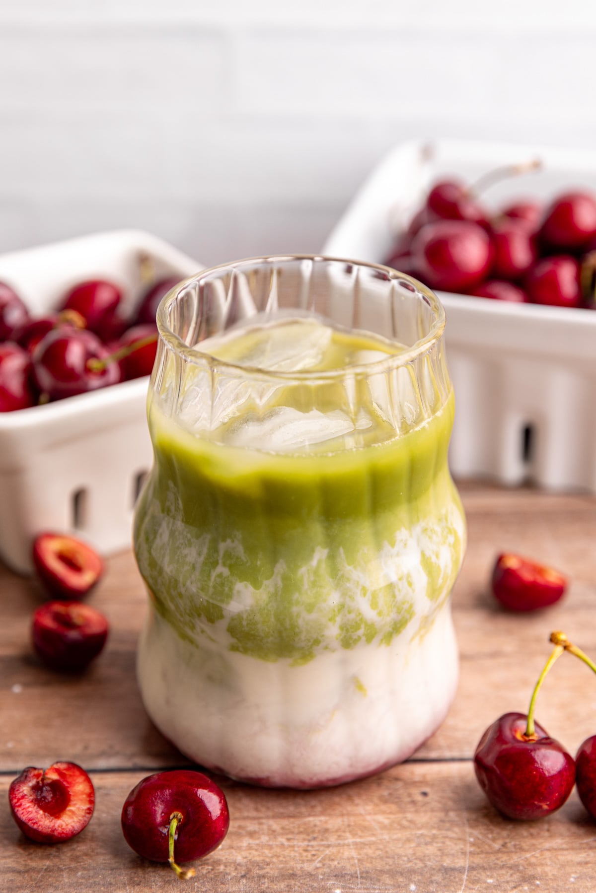 A layered matcha latte, on a countertop with berry baskets full of cherries.
