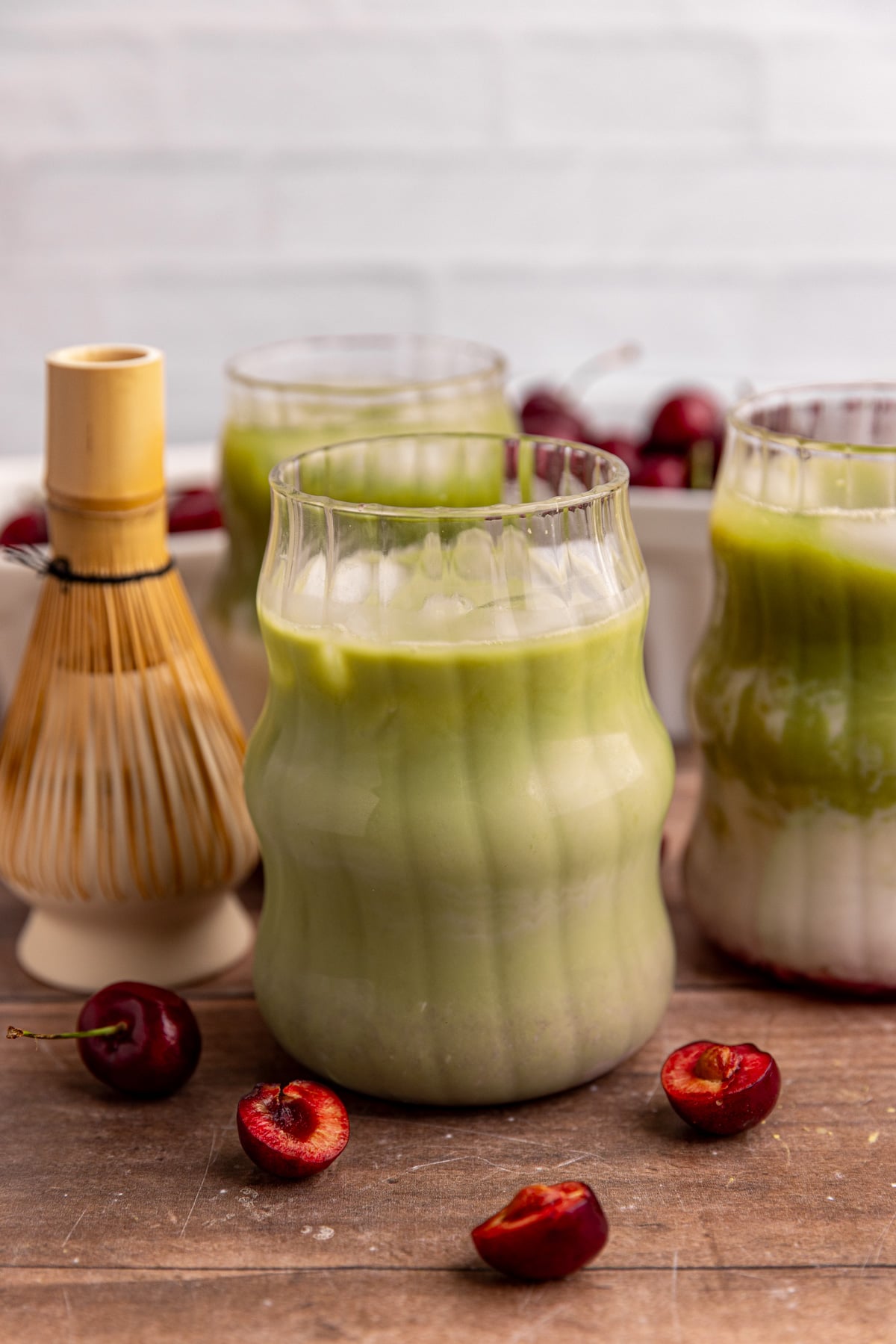 An iced cherry matcha latte, next to a matcha whisk.