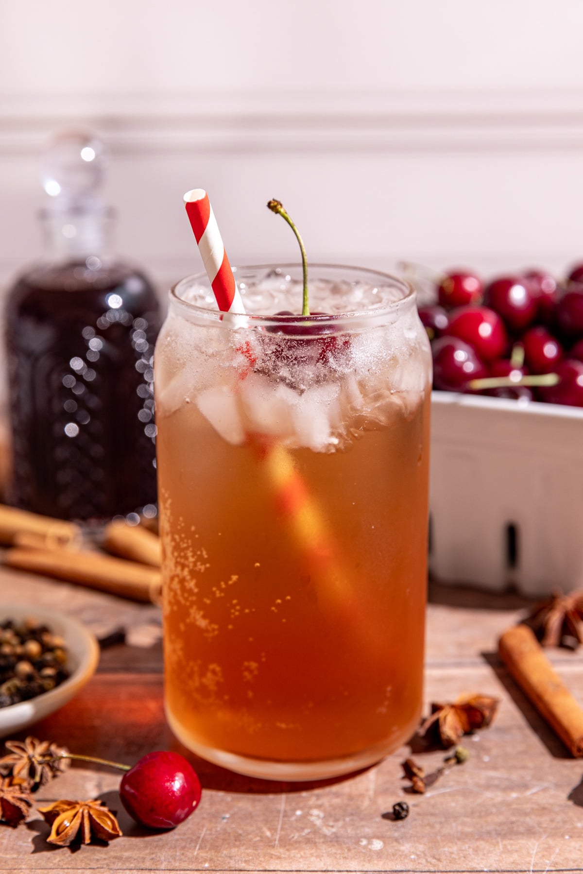 A soda glass of homemade Dr. Pepper with a cherry garnish and red & white striped straw.