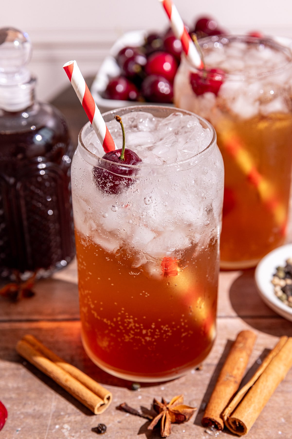 A soda glass of homemade Dr. Pepper with a cherry garnish and red & white striped straw.