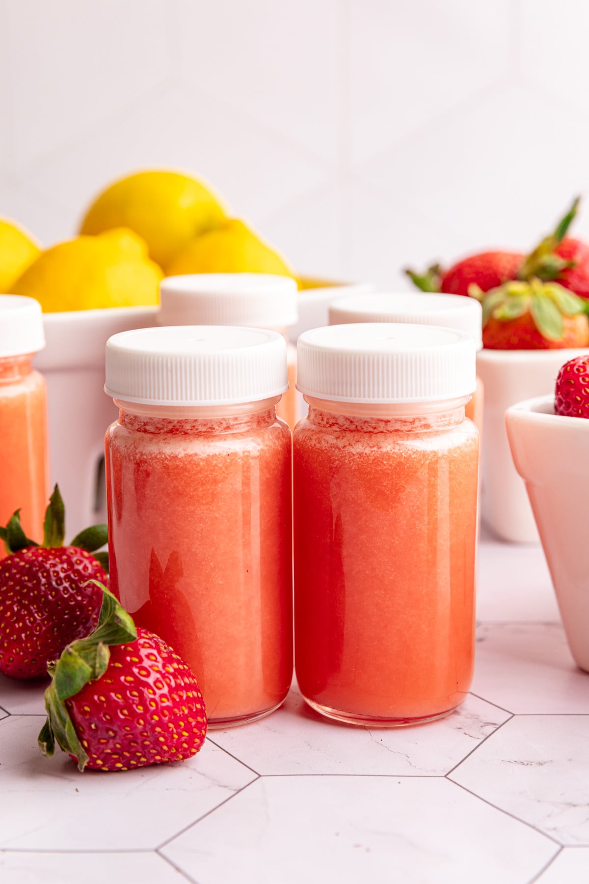 Two juice shot glasses of strawberry lemon ginger wellness shots.