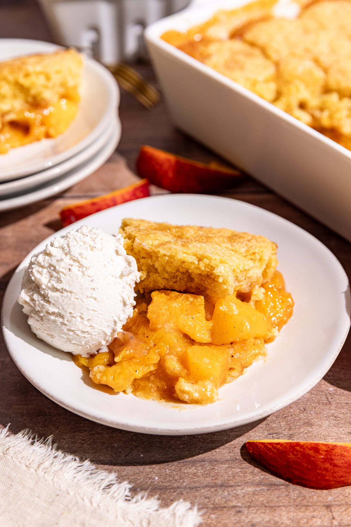 A serving of vegan cornmeal peach cobbler on a plate with a scoop of ice cream.