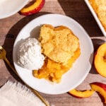 A serving of vegan cornmeal peach cobbler on a plate with a scoop of ice cream.
