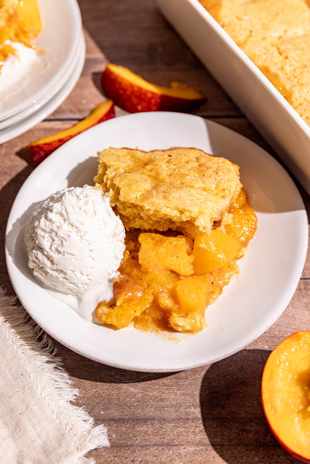 A serving of vegan cornmeal peach cobbler on a plate with a scoop of ice cream.