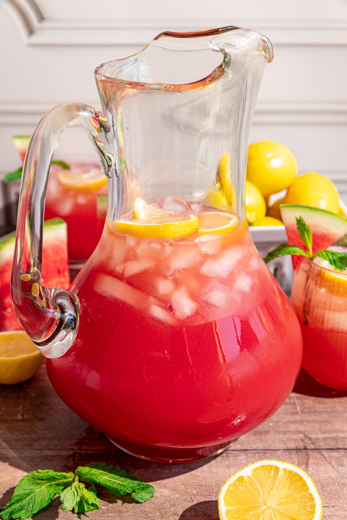 A pitcher of watermelon lemonade with lemon slices and ice.