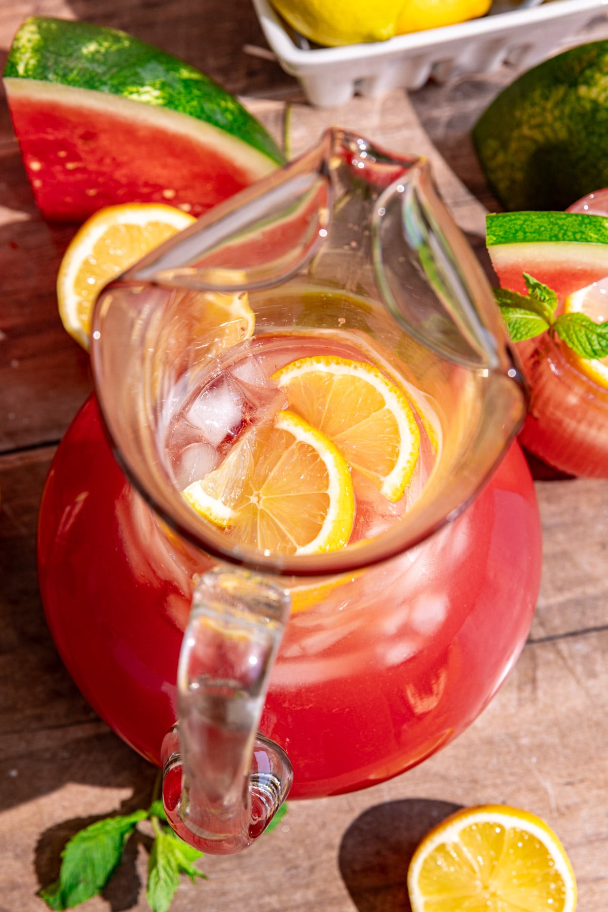A pitcher of watermelon lemonade with lemon slices and ice.