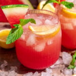 A glass of watermelon lemonade garnished with lemon, mint, and watermelon.