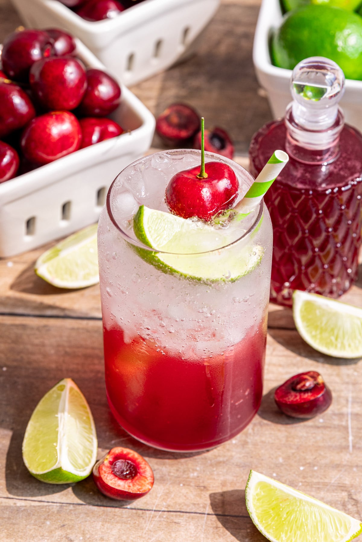 Several glasses of cherry limeade soda, garnished with a fresh cherry, lime wedge, and green and white striped straw.