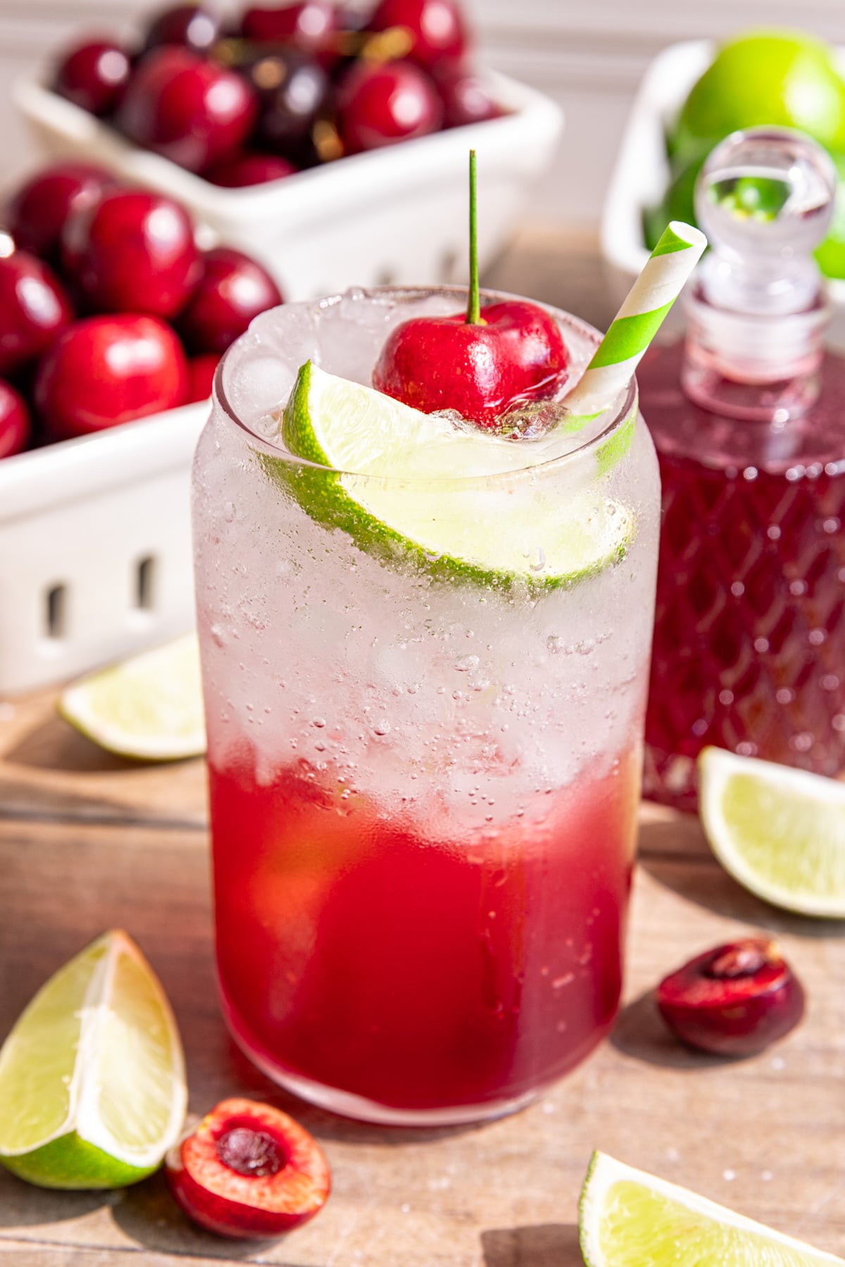Several glasses of cherry limeade soda, garnished with a fresh cherry, lime wedge, and green and white striped straw.