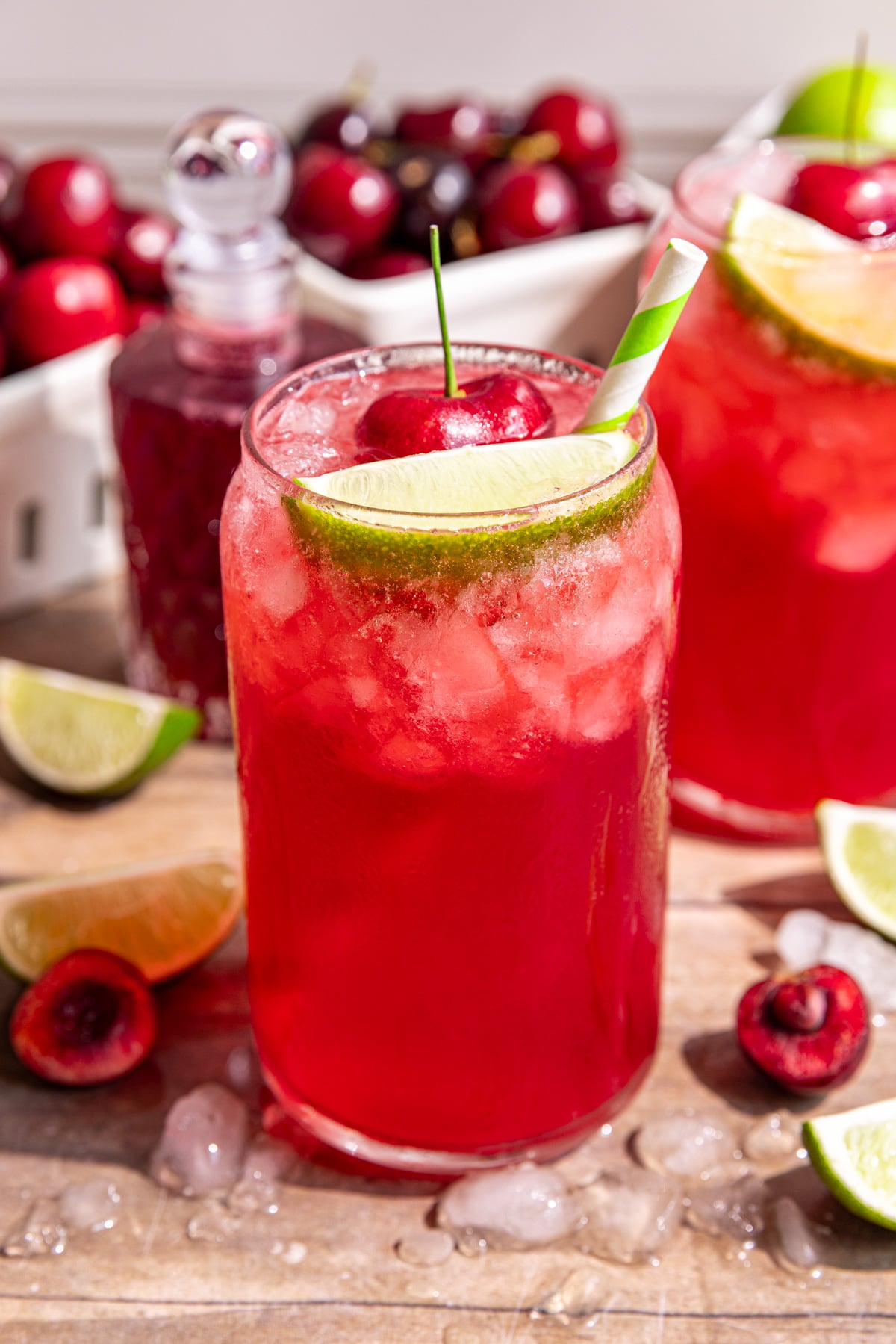 Several glasses of cherry limeade soda, garnished with a fresh cherry, lime wedge, and green and white striped straw.